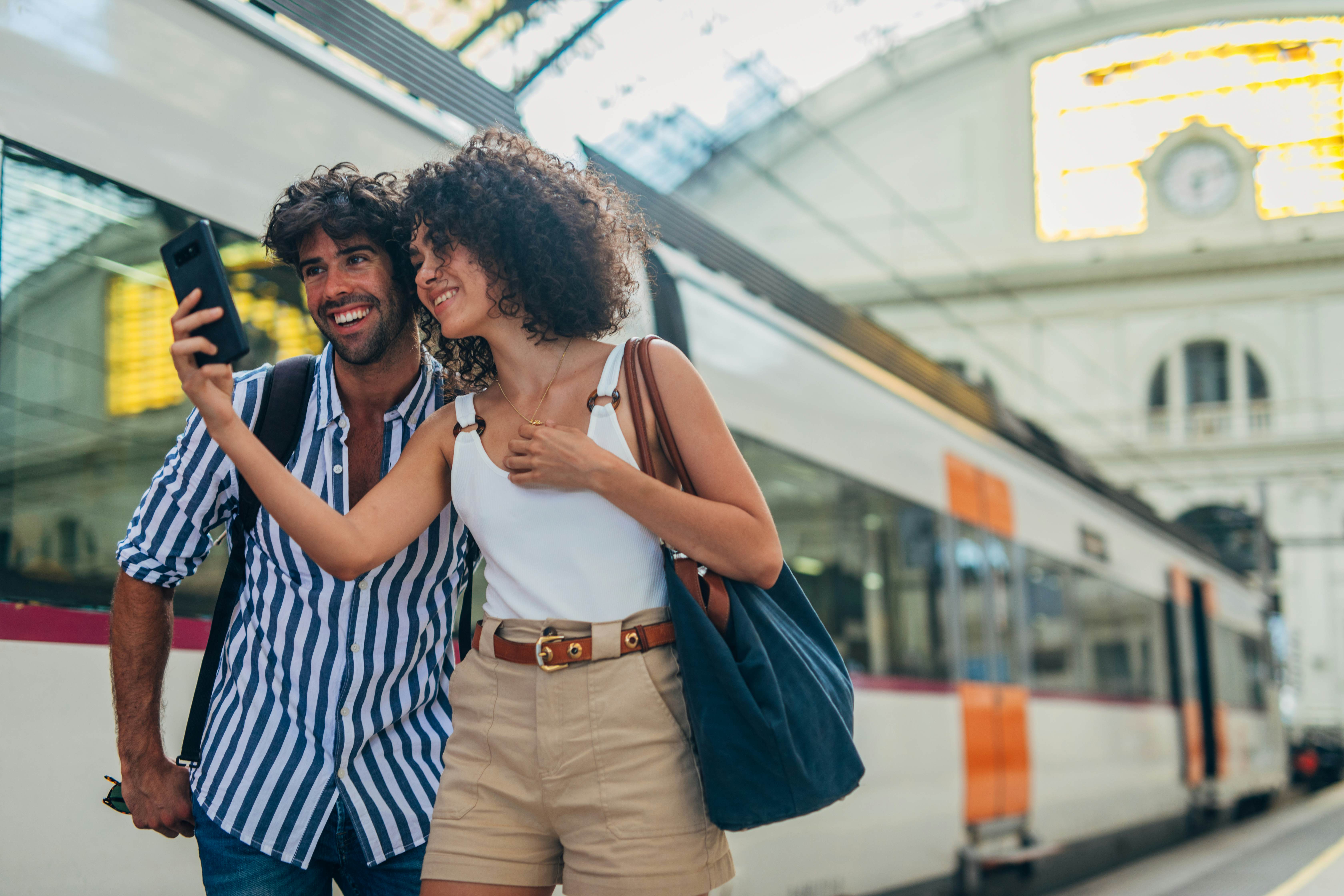 Man and woman, heterosexual couple going traveling with train together, standing on train station, using smart phone.
1170669413
Train station couple